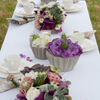 Ein Tischarrangement gestaltet von der Cacaoblüte aus violetten Hortensien und Steinblumen in geometrischen Betonbehältern.